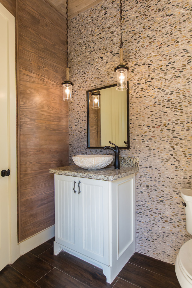 Exempel på ett mellanstort rustikt toalett, med luckor med lamellpanel, vita skåp, en toalettstol med hel cisternkåpa, flerfärgad kakel, kakel i småsten, bruna väggar, mörkt trägolv, ett fristående handfat, granitbänkskiva och brunt golv