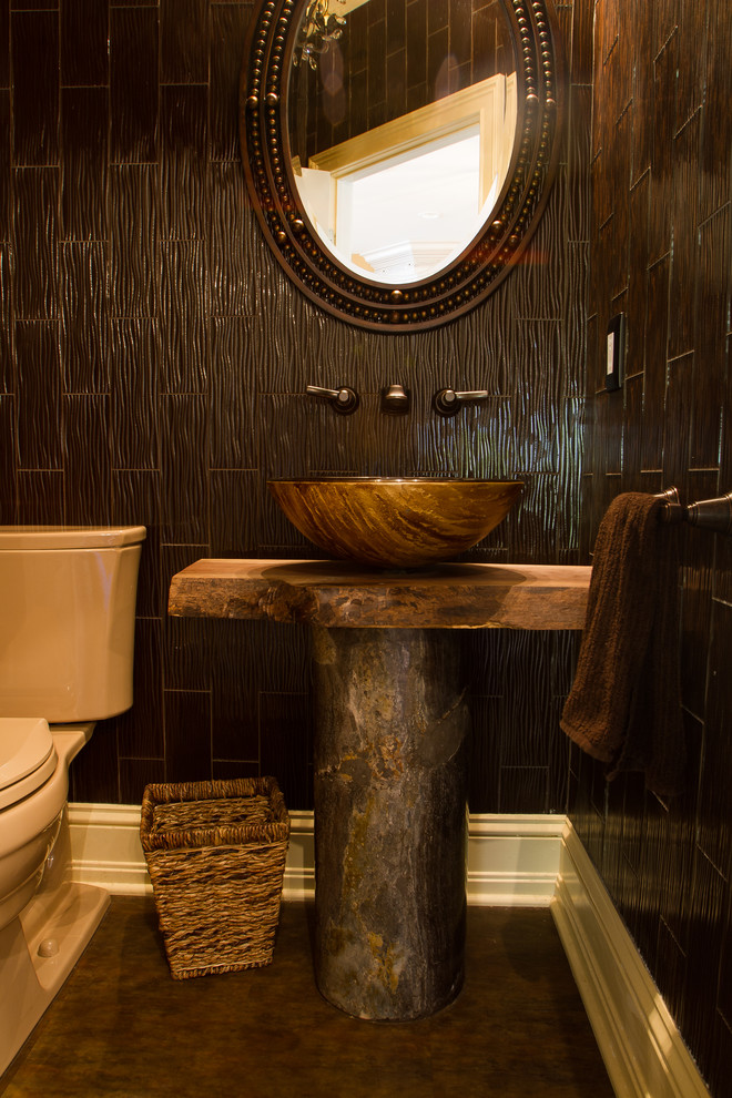 На фото: туалет в стиле рустика с настольной раковиной, искусственно-состаренными фасадами, столешницей из дерева, унитазом-моноблоком, коричневой плиткой, стеклянной плиткой, коричневыми стенами и коричневой столешницей с