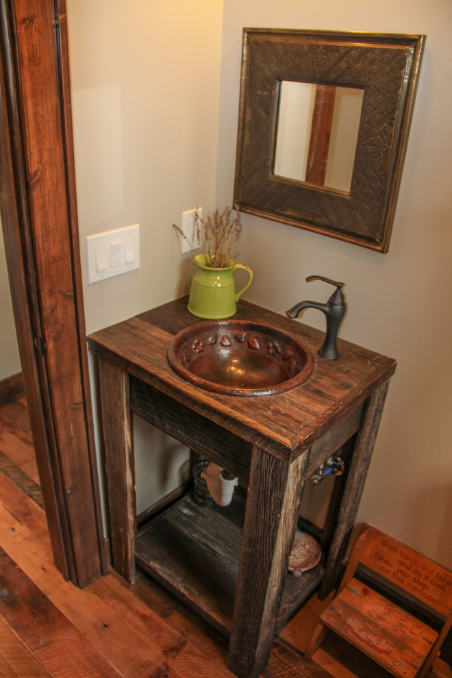 Rustik inredning av ett litet toalett, med ett nedsänkt handfat, öppna hyllor, skåp i slitet trä, träbänkskiva och mellanmörkt trägolv