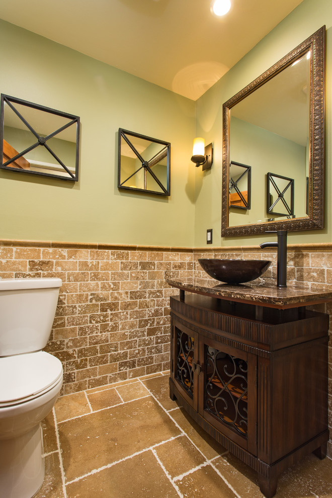 Bild på ett litet amerikanskt toalett, med möbel-liknande, skåp i mörkt trä, en toalettstol med separat cisternkåpa, beige kakel, travertinkakel, gröna väggar, travertin golv, ett fristående handfat, granitbänkskiva och brunt golv