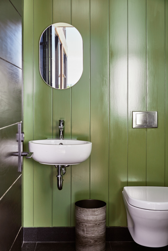 ニューヨークにあるラグジュアリーな小さなビーチスタイルのおしゃれなトイレ・洗面所 (白いキャビネット、壁掛け式トイレ、ベージュのタイル、緑の壁、大理石の床、壁付け型シンク、黒い床、白い洗面カウンター、パネル壁) の写真