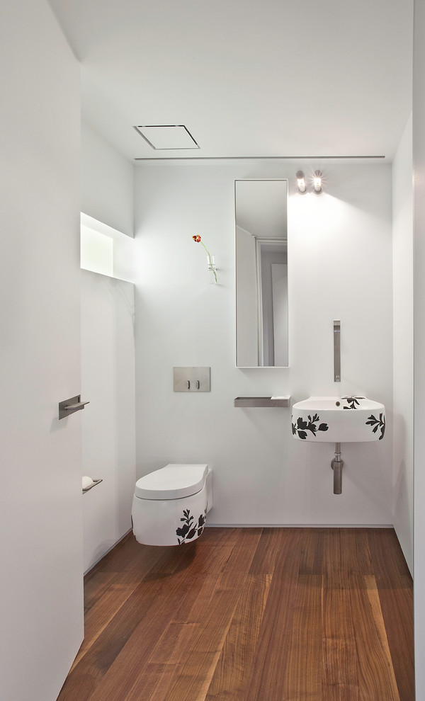 Inspiration for a mid-sized modern medium tone wood floor and brown floor powder room remodel in Salt Lake City with a wall-mount toilet, white walls and a wall-mount sink