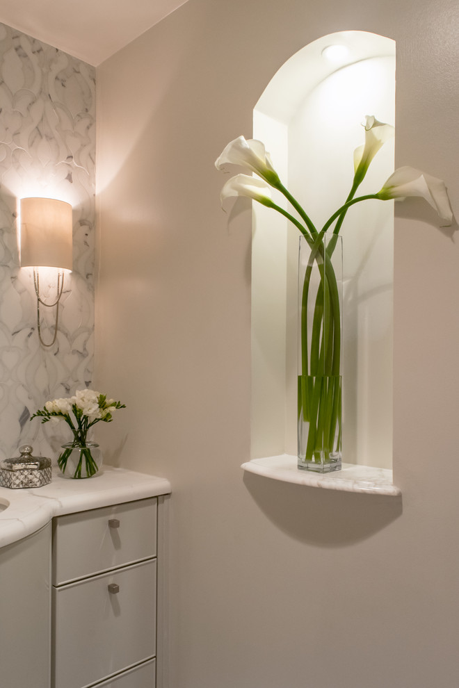 Modern inredning av ett toalett, med ett undermonterad handfat, marmorbänkskiva, vit kakel och vita väggar