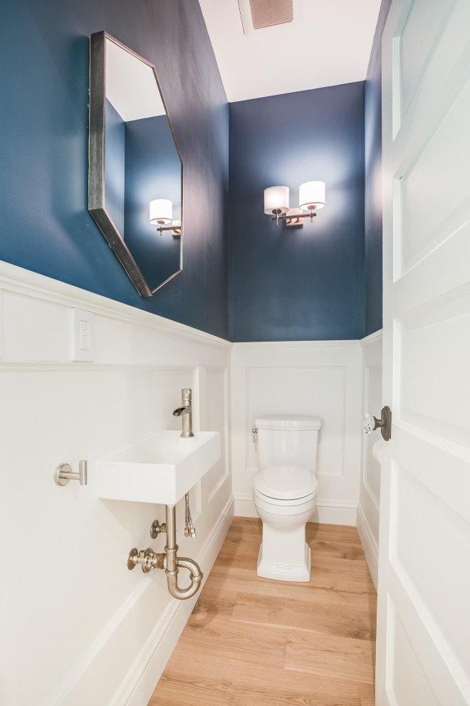 Modelo de aseo flotante clásico con puertas de armario blancas, paredes azules, suelo de madera clara, lavabo suspendido y boiserie