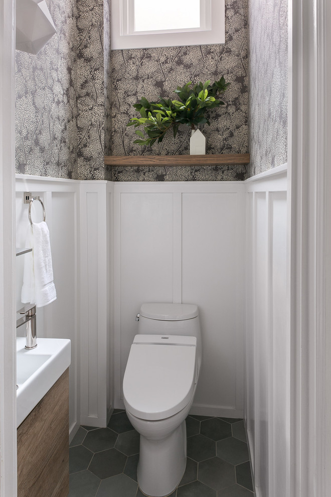На фото: туалет в стиле неоклассика (современная классика) с плоскими фасадами, фасадами цвета дерева среднего тона, унитазом-моноблоком, белыми стенами, консольной раковиной и серым полом с