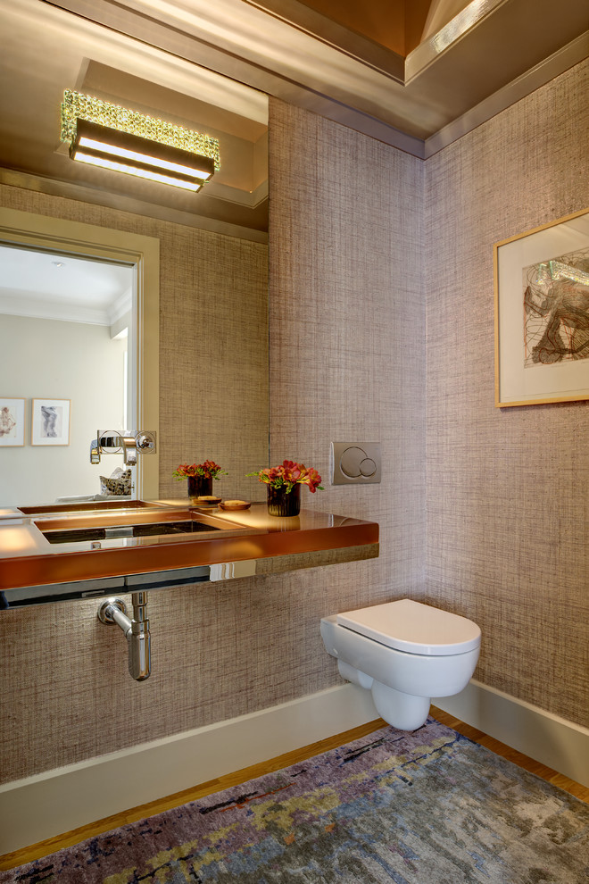 Inspiration for a small contemporary cloakroom in San Francisco with glass-front cabinets, a wall mounted toilet, pink walls, light hardwood flooring, a wall-mounted sink, glass worktops and beige floors.