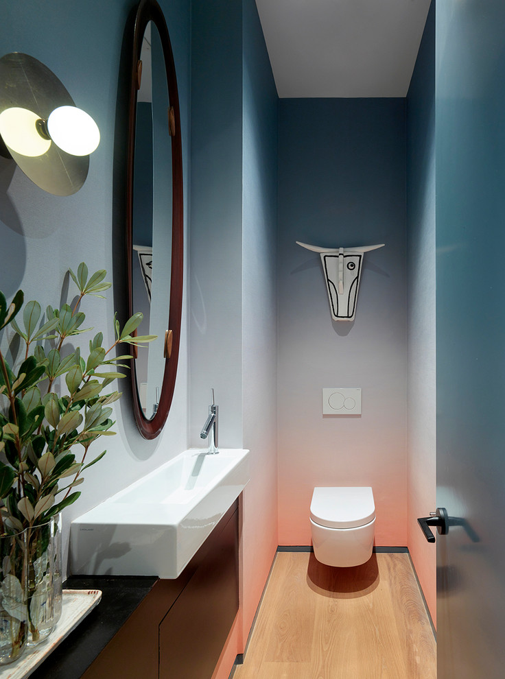 Inspiration för ett funkis toalett, med släta luckor, svarta skåp, en vägghängd toalettstol, flerfärgade väggar, mellanmörkt trägolv, ett konsol handfat och brunt golv