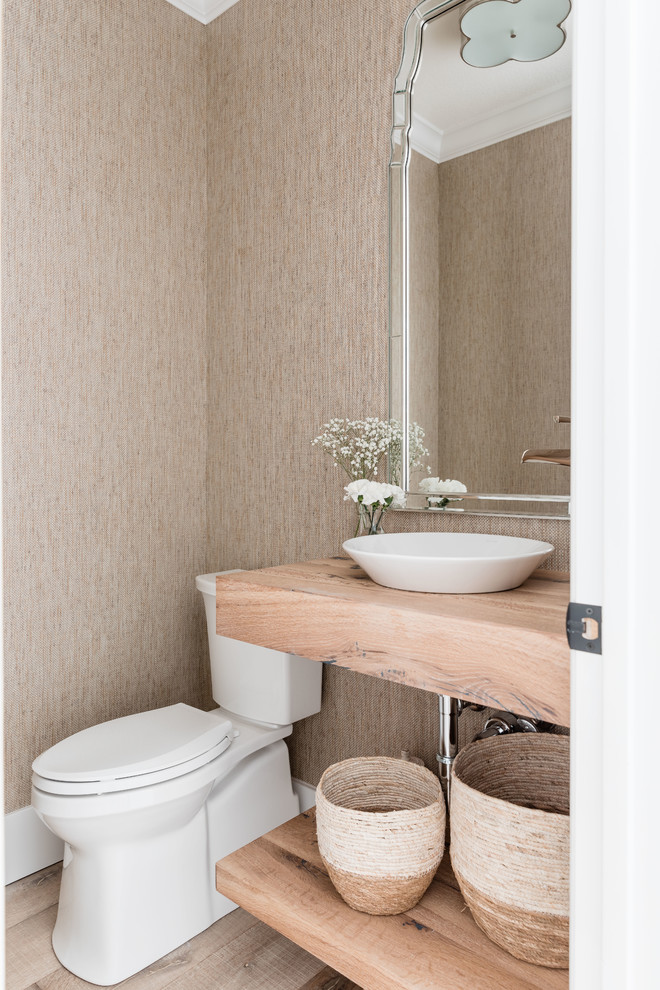 Bild på ett vintage toalett, med en toalettstol med separat cisternkåpa, beige väggar, mellanmörkt trägolv, ett fristående handfat, träbänkskiva och brunt golv