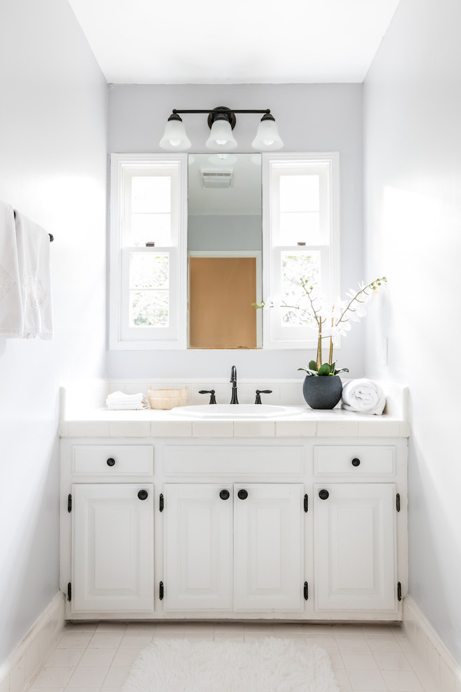 Ejemplo de aseo clásico de tamaño medio con armarios con paneles con relieve, puertas de armario blancas, lavabo encastrado y suelo blanco
