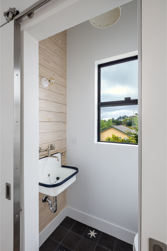 Bild på ett litet skandinaviskt toalett, med vita väggar, ett väggmonterat handfat och svart golv