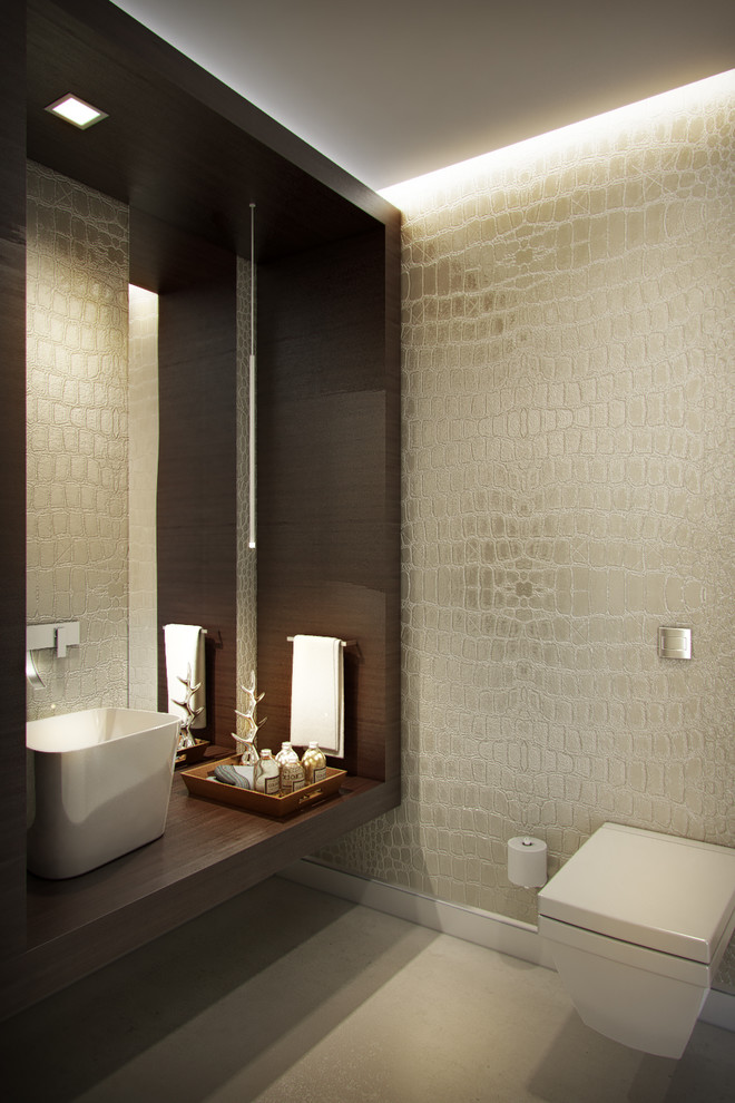 Inspiration for a medium sized contemporary cloakroom in Miami with brown cabinets, a wall mounted toilet, beige tiles, ceramic tiles, beige walls, concrete flooring, a vessel sink, wooden worktops, beige floors, brown worktops and feature lighting.