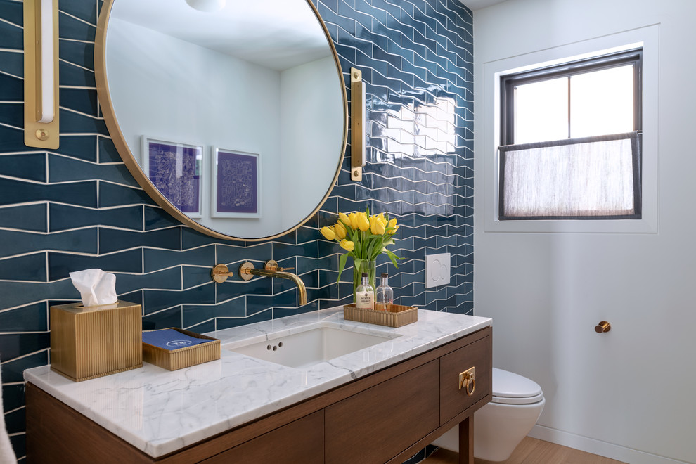 Cette image montre un WC suspendu rustique en bois foncé avec un placard en trompe-l'oeil, un carrelage bleu, un mur blanc, parquet clair, un lavabo encastré et un plan de toilette blanc.