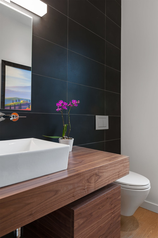 Cette photo montre un WC suspendu scandinave de taille moyenne avec des portes de placard noires, un carrelage noir, des carreaux de céramique, un mur multicolore, un sol en bois brun, une vasque, un plan de toilette en bois, un sol marron et un plan de toilette marron.