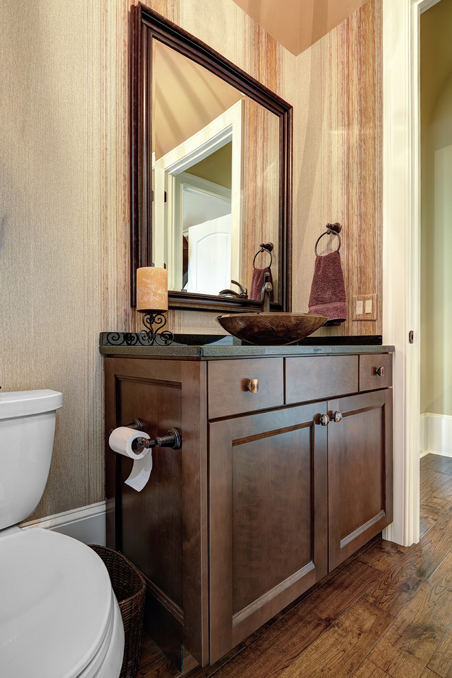 Design ideas for a medium sized classic cloakroom in Charleston with a two-piece toilet, dark hardwood flooring, a vessel sink, brown floors, a built in vanity unit, wallpapered walls, dark wood cabinets and black worktops.