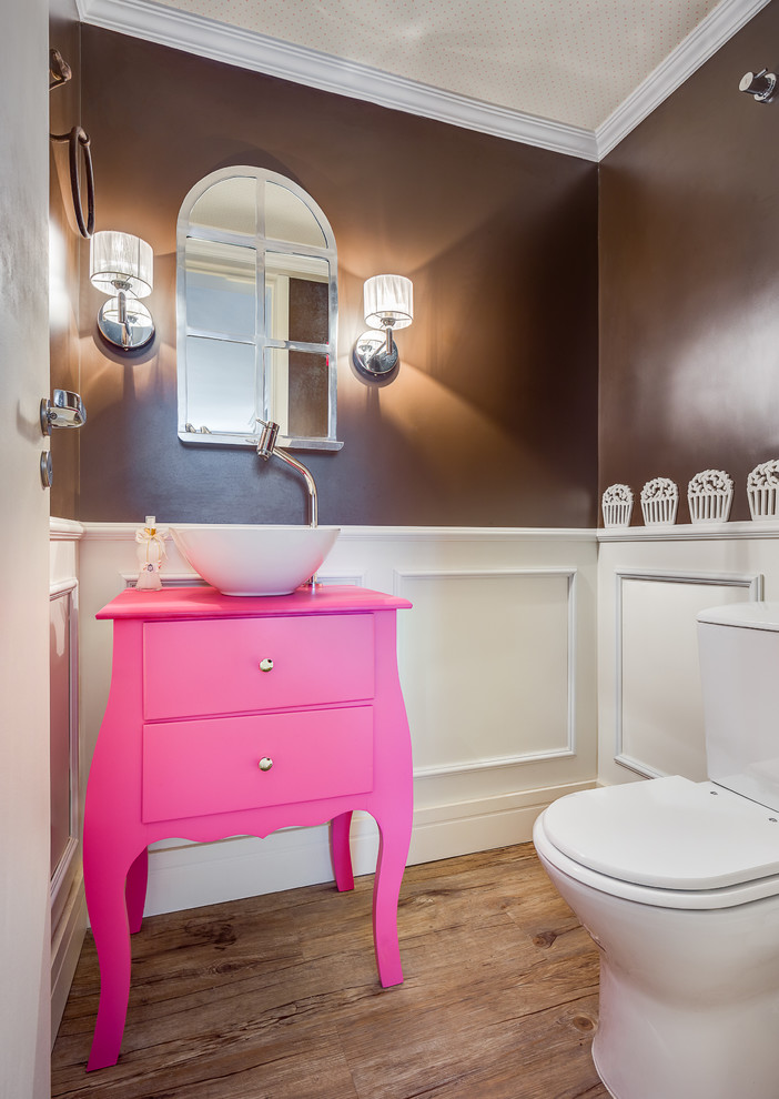 Inredning av ett litet rosa rosa toalett, med ett nedsänkt handfat, möbel-liknande, träbänkskiva, en toalettstol med hel cisternkåpa, flerfärgade väggar och vinylgolv