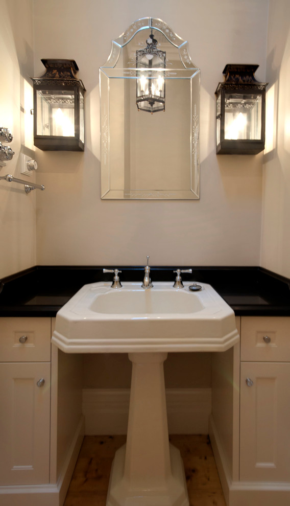 Cette image montre un grand WC et toilettes traditionnel avec un placard à porte shaker, un plan de toilette en granite, WC à poser, un sol en bois brun, un plan vasque, des portes de placard blanches et un mur beige.