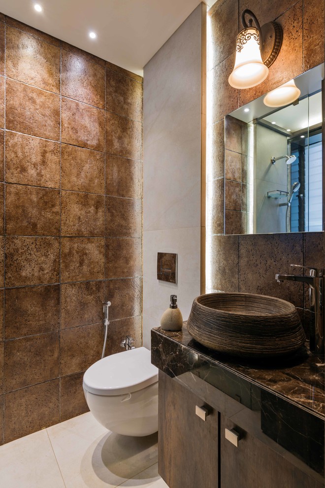 Inspiration for a small mediterranean cloakroom in Mumbai with freestanding cabinets, brown cabinets, a wall mounted toilet, brown tiles, brown walls, a vessel sink, white floors and brown worktops.