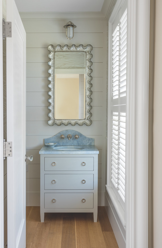 Photo of a medium sized nautical cloakroom in Portland Maine with freestanding cabinets, white cabinets, white tiles, white walls, light hardwood flooring, a console sink, quartz worktops, brown floors and blue worktops.