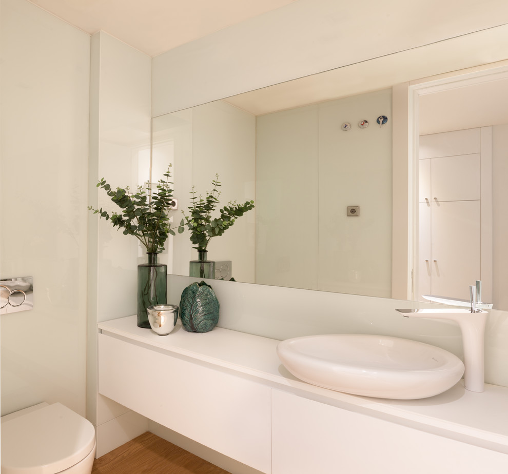 Idées déco pour un WC suspendu contemporain de taille moyenne avec un placard à porte plane, des portes de placard blanches, un mur blanc, un sol en bois brun et une vasque.