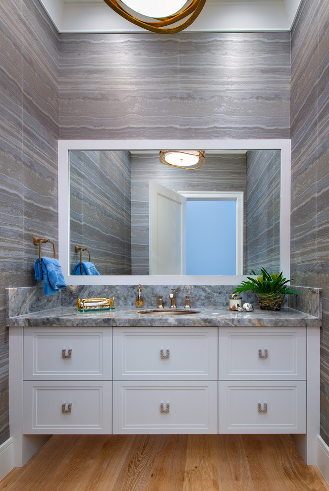 Inredning av ett klassiskt grå grått toalett, med luckor med infälld panel, vita skåp, grå väggar, ljust trägolv, ett undermonterad handfat och beiget golv