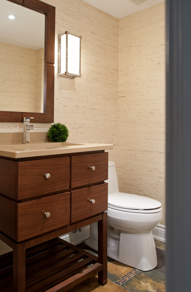 Inredning av ett modernt litet toalett, med ett undermonterad handfat, släta luckor, skåp i mellenmörkt trä, bänkskiva i kvarts, en toalettstol med hel cisternkåpa, beige väggar och skiffergolv