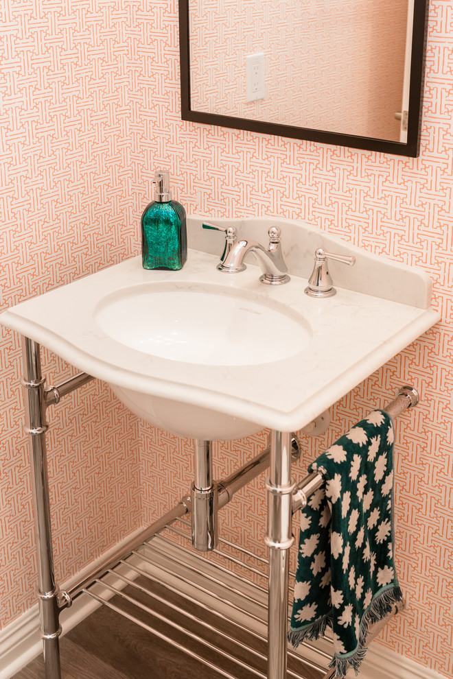Foto på ett funkis vit toalett, med en toalettstol med separat cisternkåpa, orange väggar, laminatgolv, ett undermonterad handfat, bänkskiva i kvarts och grått golv