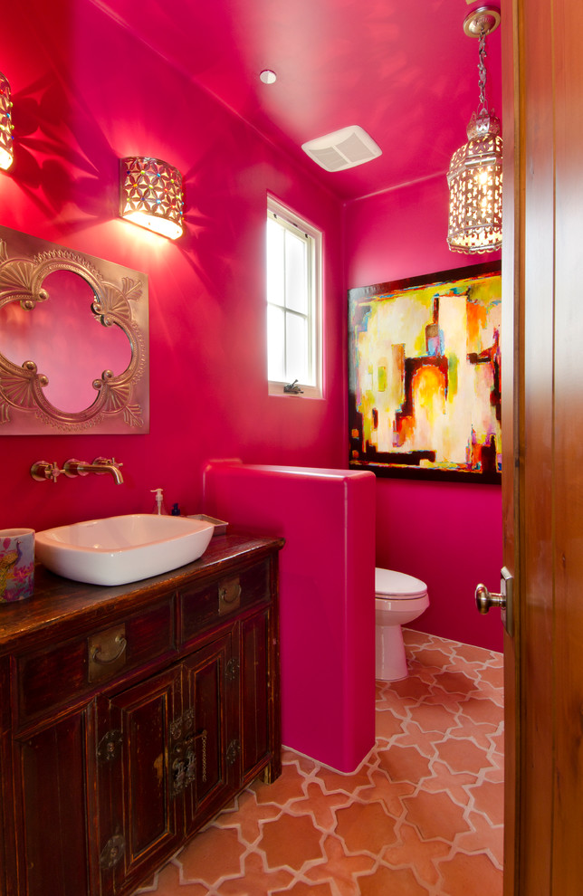 Foto de aseo de estilo americano de tamaño medio con lavabo sobreencimera, armarios tipo mueble, puertas de armario de madera en tonos medios, sanitario de una pieza, paredes rosas y suelo de baldosas de terracota