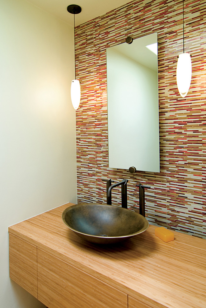 Cette image montre un petit WC et toilettes design en bois clair avec une vasque, un placard à porte plane, un plan de toilette en bois, un carrelage multicolore, un mur beige, des carreaux en allumettes et un plan de toilette marron.