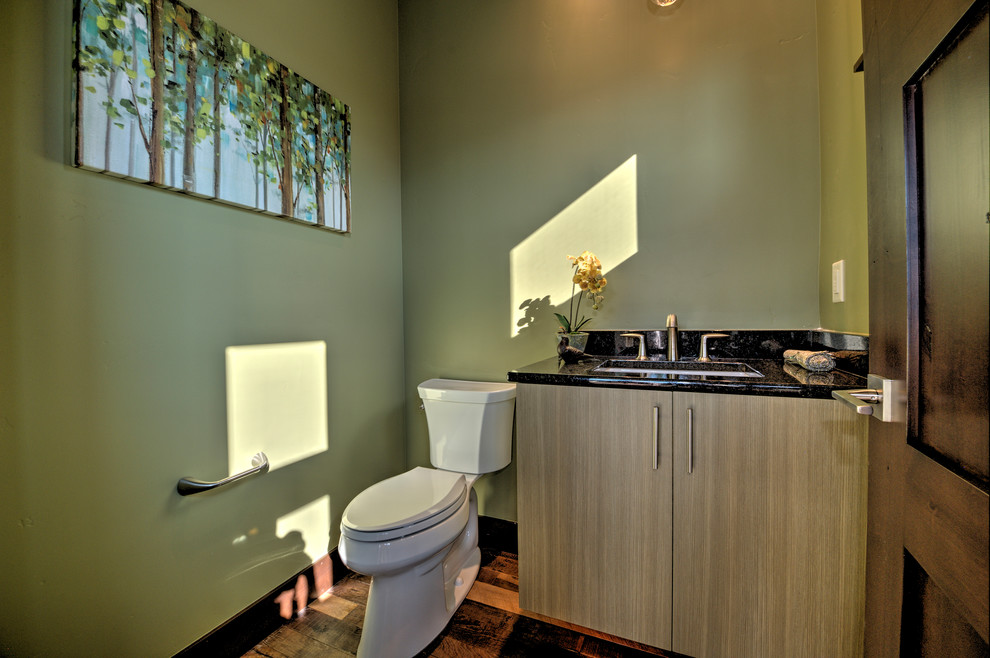 Cette image montre un petit WC et toilettes design en bois clair avec un lavabo encastré, un placard à porte plane, un plan de toilette en granite, WC séparés, un mur vert et un sol en bois brun.