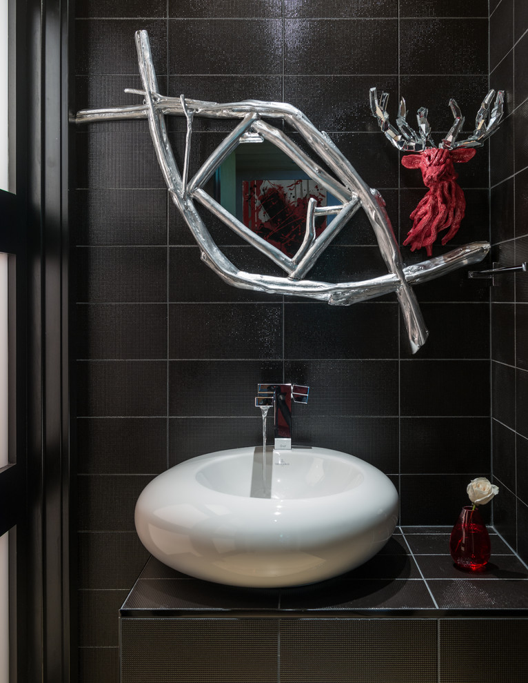 他の地域にある高級なコンテンポラリースタイルのおしゃれなトイレ・洗面所 (ベッセル式洗面器、タイルの洗面台、黒いタイル、黒い壁) の写真