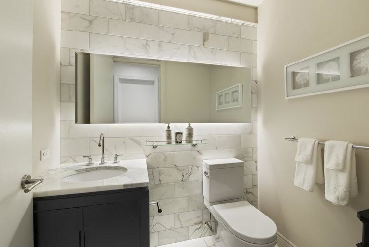 Cette image montre un petit WC et toilettes design avec un placard avec porte à panneau encastré, des portes de placard noires, WC à poser, un carrelage blanc, du carrelage en marbre, un mur blanc, un sol en marbre, un lavabo encastré, un plan de toilette en marbre et un sol blanc.