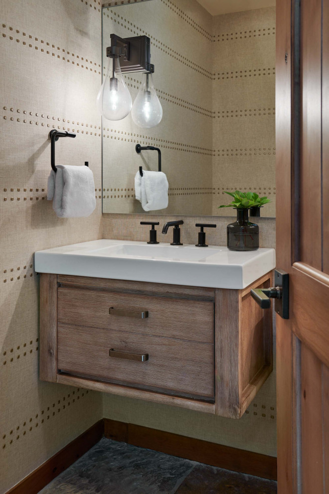 Photo of a small rustic cloakroom in Denver with flat-panel cabinets, medium wood cabinets, a two-piece toilet, beige walls, slate flooring, an integrated sink, solid surface worktops, grey floors, white worktops, a floating vanity unit and wallpapered walls.