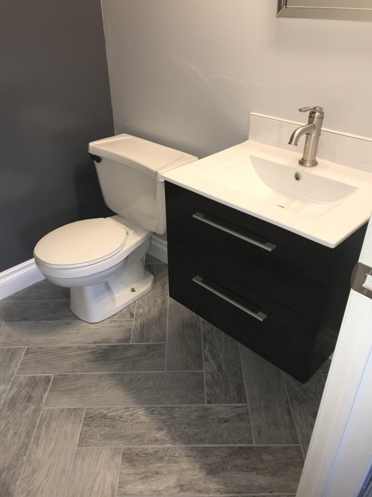 Idee per un piccolo bagno di servizio moderno con ante nere, WC a due pezzi, pareti grigie, pavimento con piastrelle in ceramica, lavabo sospeso, top in granito, pavimento grigio, top bianco e mobile bagno sospeso