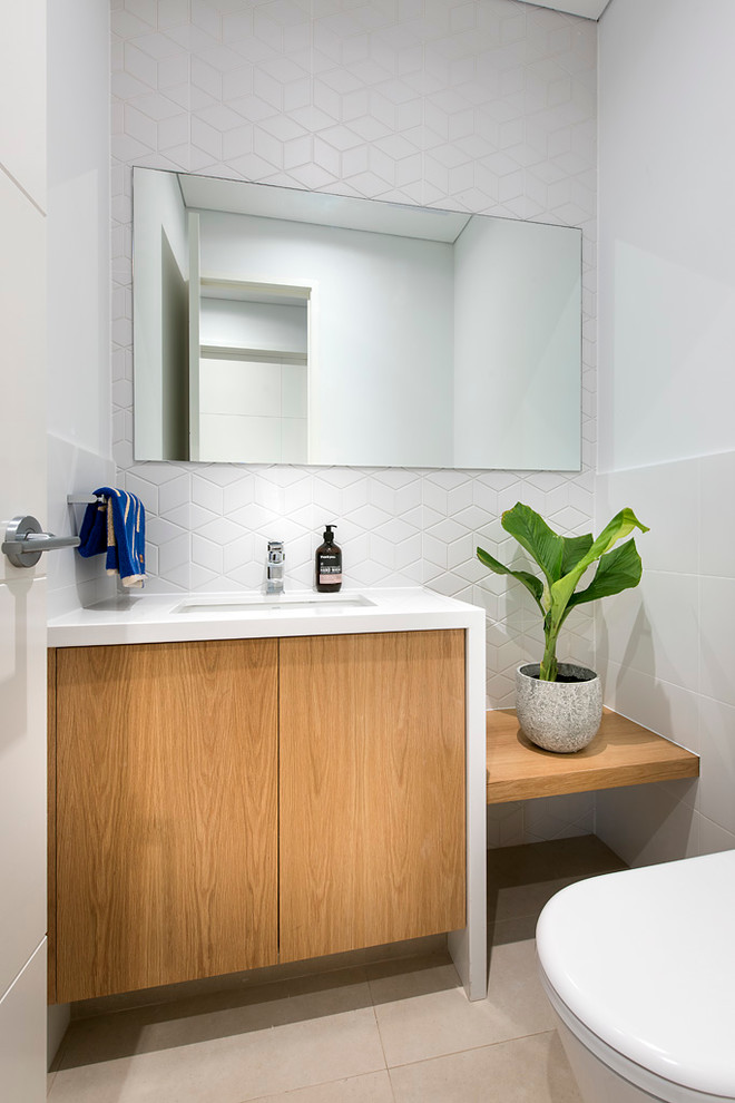 Cette photo montre un petit WC et toilettes tendance en bois clair avec un lavabo encastré, un plan de toilette en quartz modifié, un carrelage blanc, des carreaux de porcelaine, un mur blanc, un sol en carrelage de porcelaine et un plan de toilette blanc.