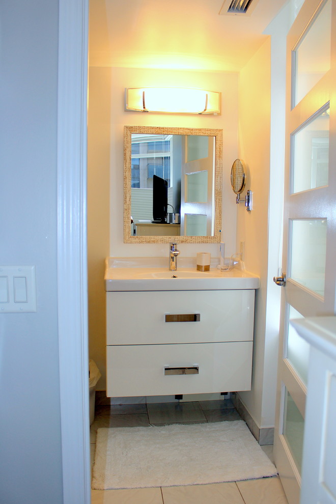 Cette photo montre un petit WC et toilettes chic avec un carrelage blanc, des carreaux de porcelaine, un mur blanc, un sol en carrelage de porcelaine, un lavabo intégré, un placard à porte plane et des portes de placard blanches.