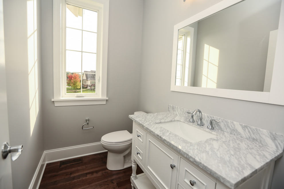 Inspiration for a mid-sized transitional powder room remodel in New York with furniture-like cabinets, white cabinets, a two-piece toilet, gray walls, an undermount sink and marble countertops