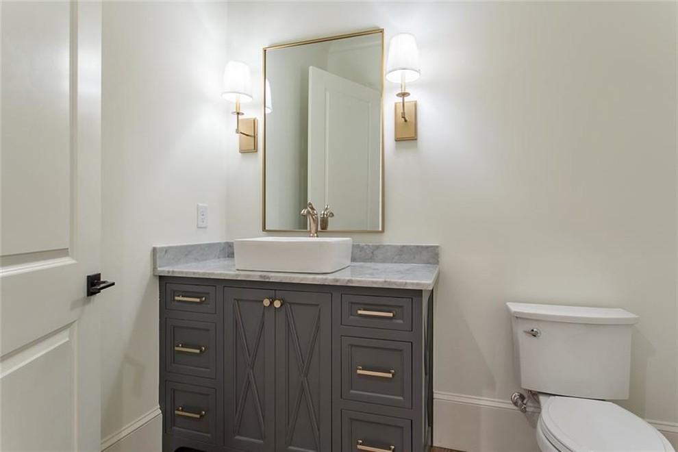 Inspiration for a mid-sized transitional light wood floor and gray floor powder room remodel in Atlanta with recessed-panel cabinets, gray cabinets, a two-piece toilet, white walls, a vessel sink, marble countertops and gray countertops