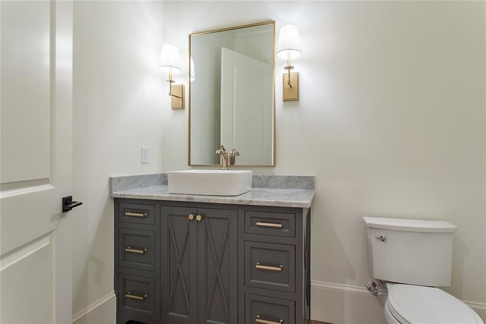 Photo of a medium sized traditional cloakroom in Atlanta with recessed-panel cabinets, grey cabinets, a two-piece toilet, white walls, light hardwood flooring, a vessel sink, marble worktops, grey floors and grey worktops.
