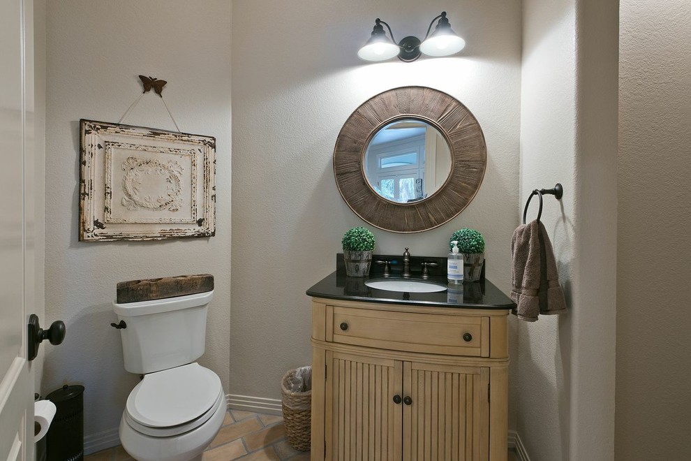 Cette image montre un petit WC et toilettes traditionnel en bois clair avec un lavabo encastré, un placard en trompe-l'oeil, un plan de toilette en granite, WC séparés, un mur beige, un sol en brique et un sol beige.