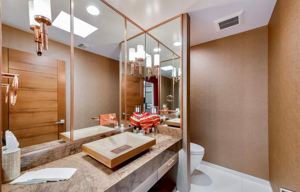 Large contemporary cloakroom in Los Angeles with flat-panel cabinets, light wood cabinets, a one-piece toilet, brown walls, limestone flooring, a vessel sink, onyx worktops, white floors, brown worktops, a built in vanity unit and wallpapered walls.