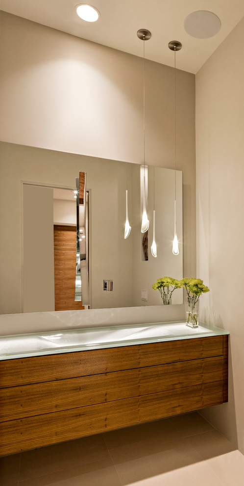 Photo of a large modern cloakroom in Phoenix with flat-panel cabinets, medium wood cabinets, a one-piece toilet, glass sheet walls, beige walls, ceramic flooring, a built-in sink and glass worktops.