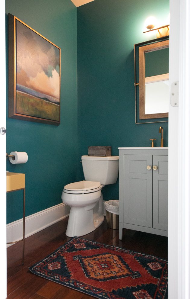 Réalisation d'un petit WC et toilettes design avec un placard à porte shaker, des portes de placard grises, un mur vert, un sol en bois brun, un sol marron et un plan de toilette blanc.
