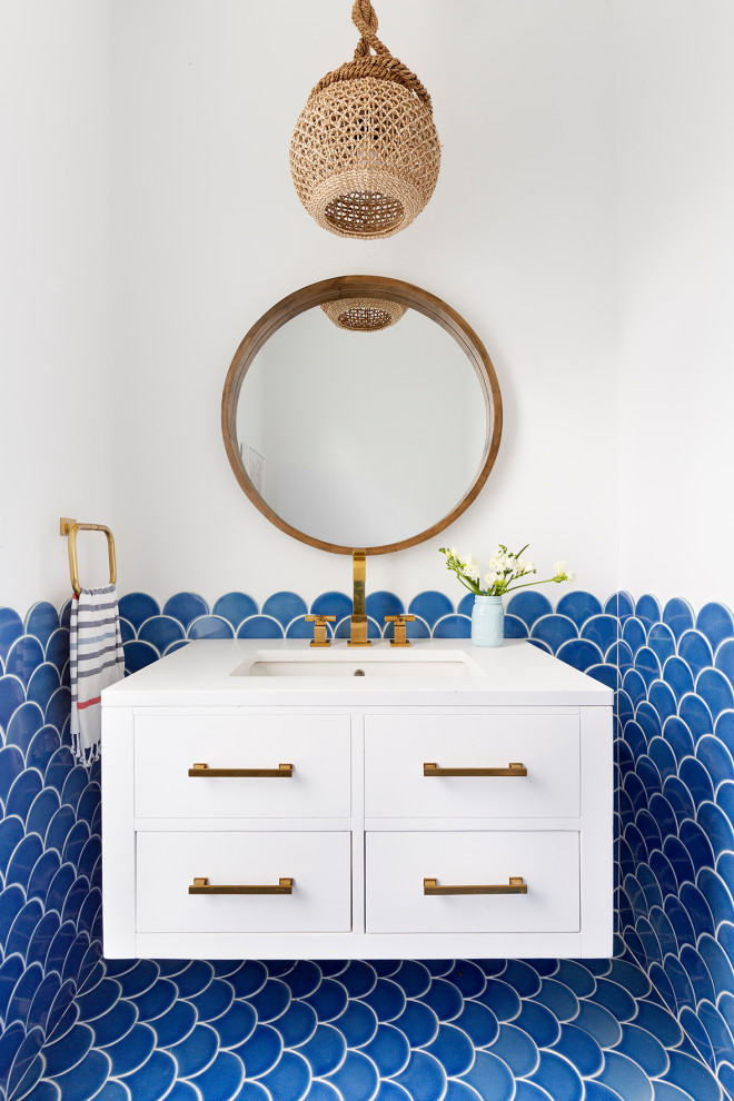 Photo of a beach style cloakroom in New York with flat-panel cabinets, white cabinets, blue tiles, white walls, a submerged sink, blue floors and white worktops.