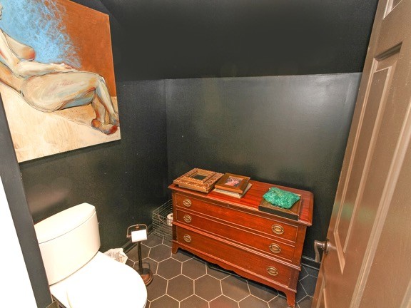 Bild på ett litet lantligt toalett, med möbel-liknande, skåp i mörkt trä, en toalettstol med separat cisternkåpa, svarta väggar, klinkergolv i porslin och grått golv