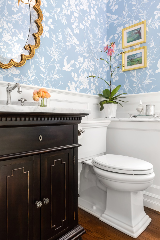 Foto di un bagno di servizio classico di medie dimensioni con consolle stile comò, ante nere, WC a due pezzi, pareti blu, pavimento in legno massello medio, lavabo sottopiano, top in marmo e pavimento marrone