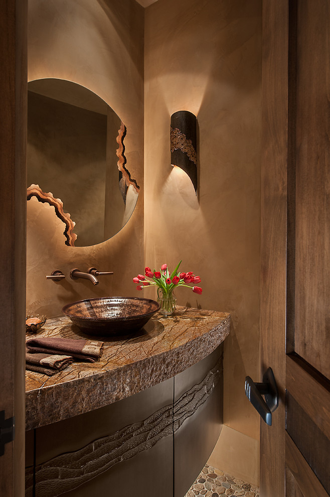 Aménagement d'un WC et toilettes sud-ouest américain en bois foncé de taille moyenne avec une vasque, un placard en trompe-l'oeil, un plan de toilette en granite, un mur beige et un sol en galet.