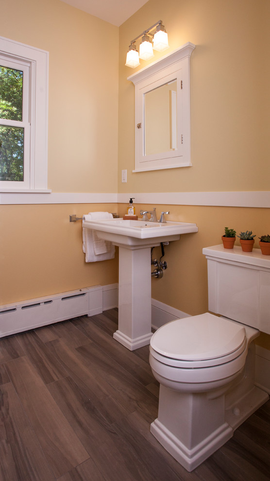Foto di un piccolo bagno di servizio chic con WC a due pezzi, pareti gialle, pavimento in legno massello medio, lavabo a colonna e pavimento marrone