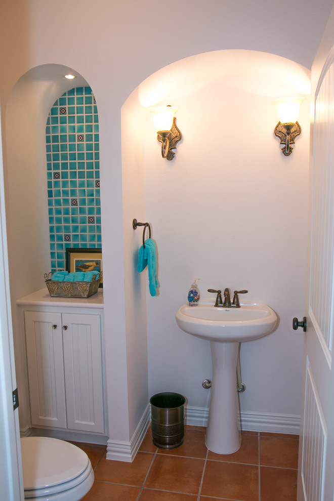 Photo of a medium sized cloakroom in Austin with recessed-panel cabinets, white cabinets, a two-piece toilet, terracotta tiles, white walls, terracotta flooring, a pedestal sink, solid surface worktops, orange floors and white worktops.