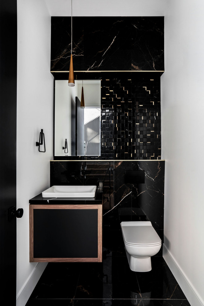 Inredning av ett modernt toalett, med släta luckor, svarta skåp, en toalettstol med hel cisternkåpa, vita väggar, ett fristående handfat och svart golv