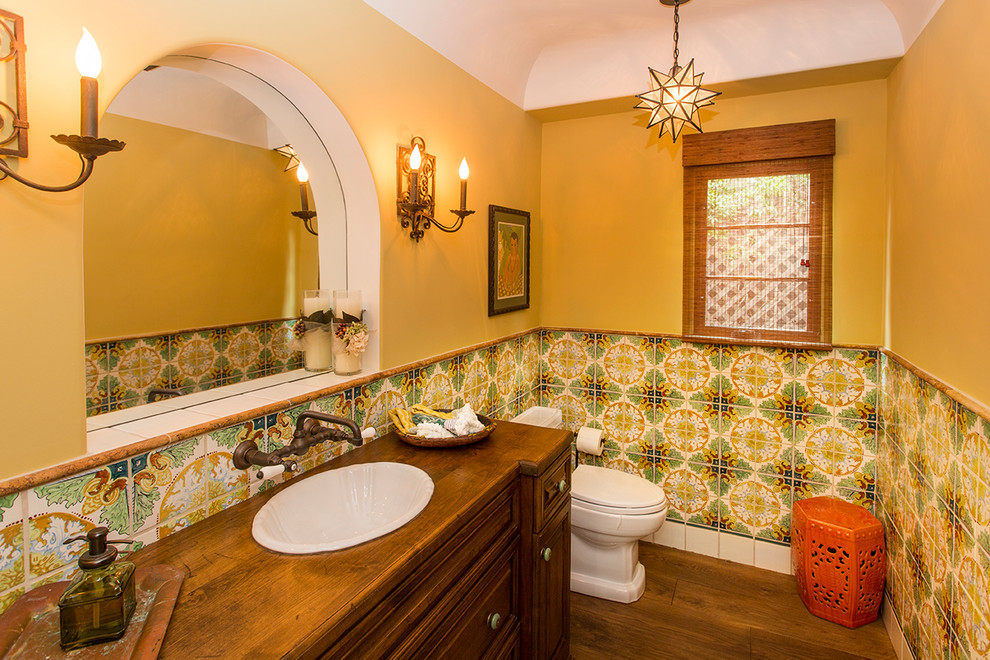 Foto di un bagno di servizio mediterraneo con ante in legno bruno, WC a due pezzi, piastrelle multicolore, pareti gialle e parquet scuro